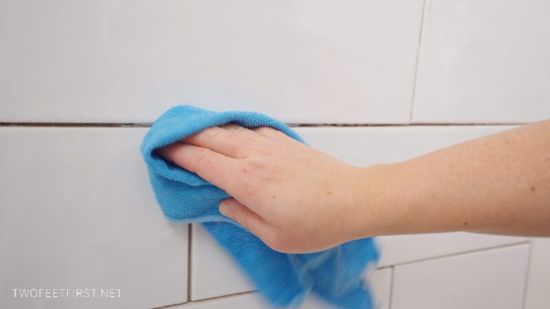 using microfiber towel to remove dust on white tiled shower walls