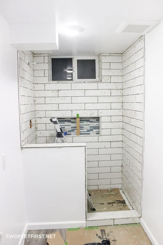 tiling shower with white tiles and grey mortar